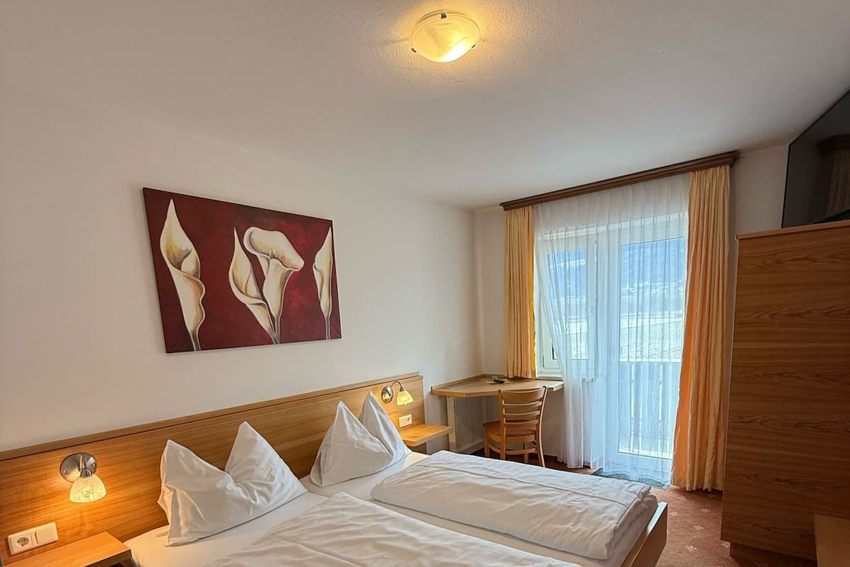 A hotel room with two beds, a desk, a chair, a painting, and a ceiling light.