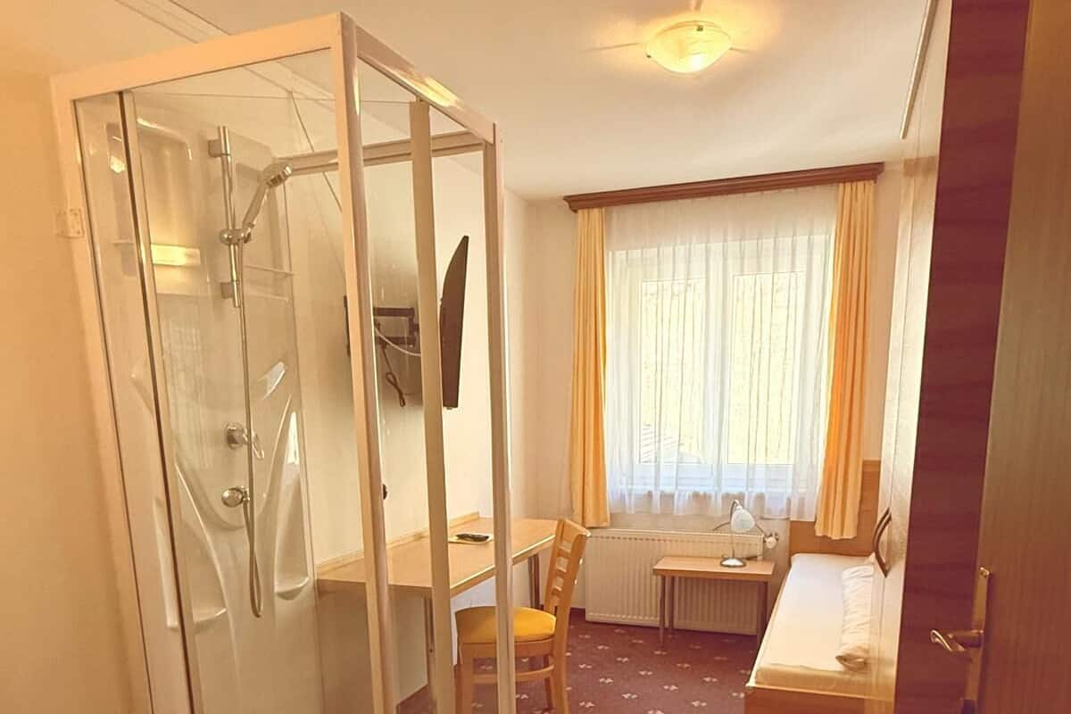 A compact hotel room with a shower, a small table, a chair, and a bed.