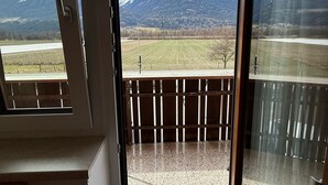 A room with a sliding glass door leading to a balcony with a view of snow-capped mountains and a field. - Pension Plattenhof  (Telfs)