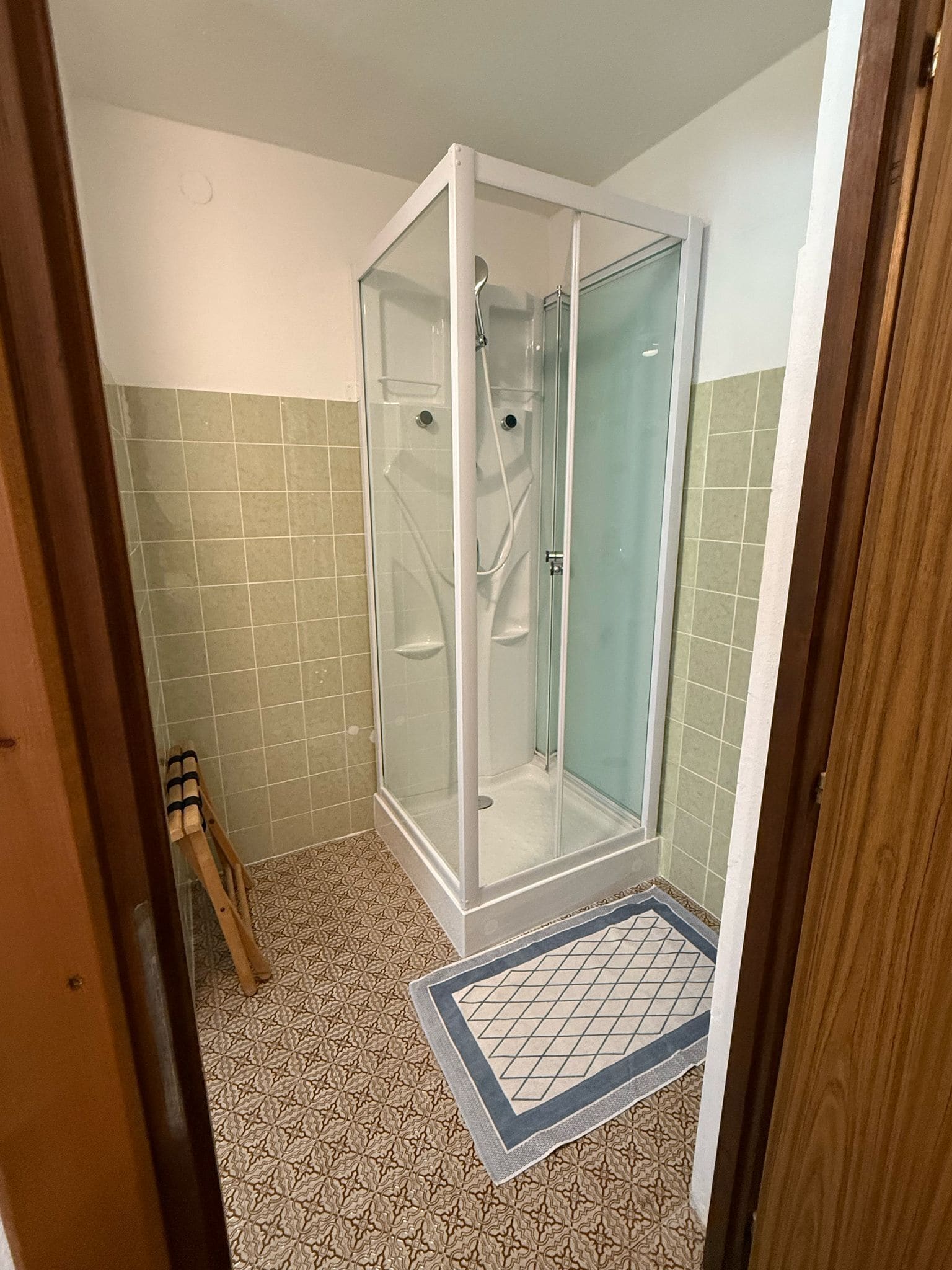 A bathroom with a glass-enclosed shower, patterned floor tiles, and a wooden door frame.