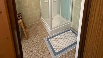 A bathroom with a glass-enclosed shower, patterned floor tiles, and a wooden door frame.