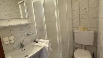 A bathroom with a shower, sink, toilet, and a blue trash bin.