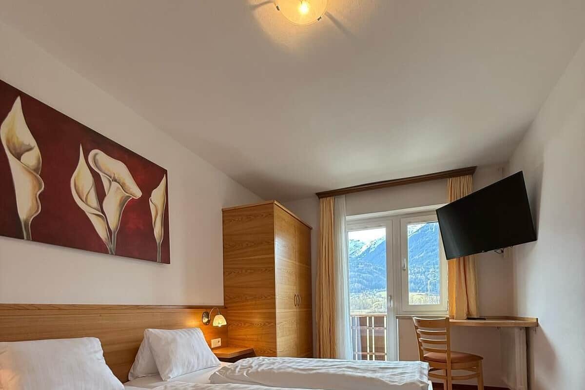 A hotel room with a large bed, a desk, a TV, and a painting on the wall.