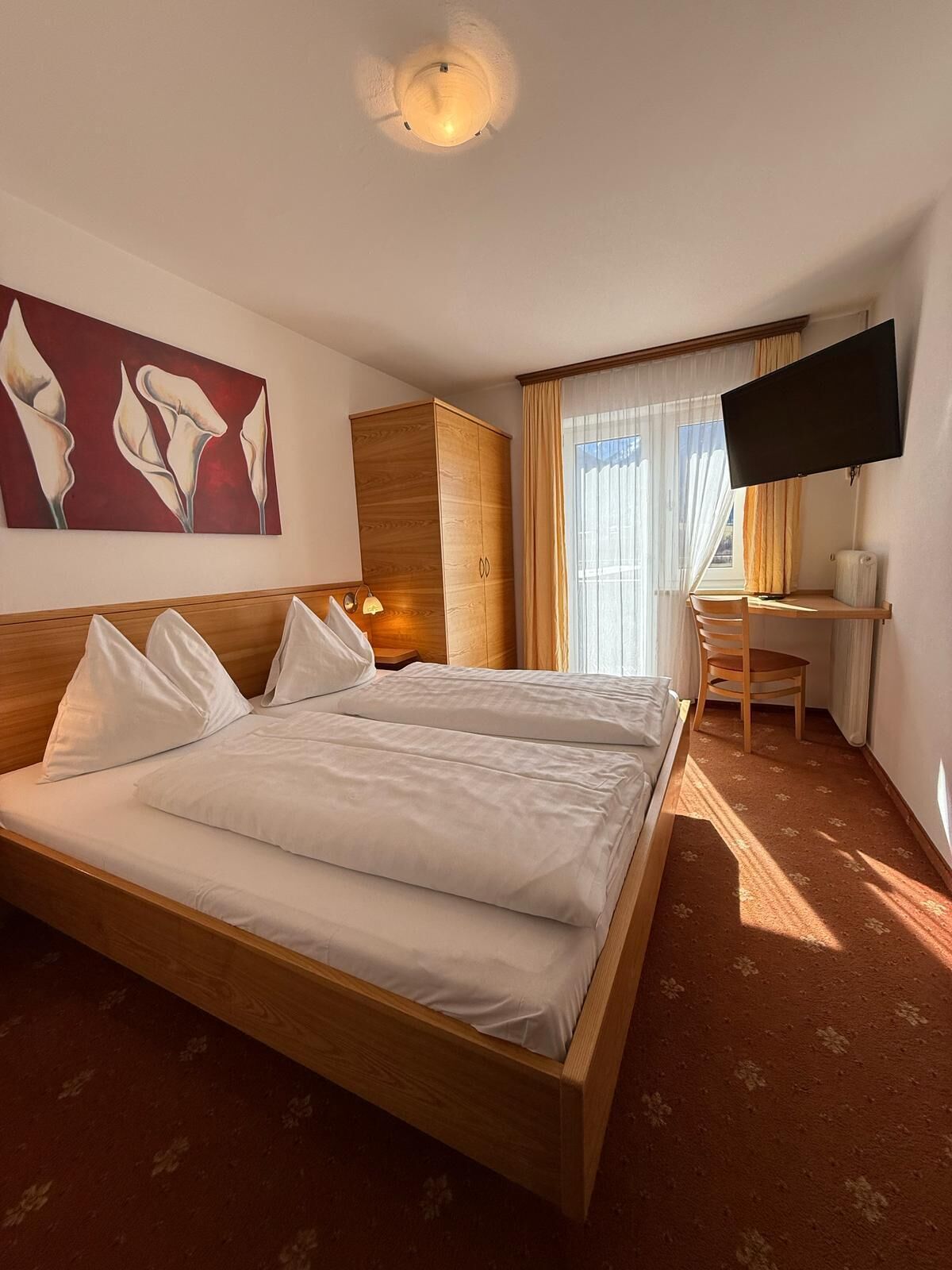 Una habitación de hotel con una cama grande, un escritorio con una silla, un televisor y un cuadro en la pared.