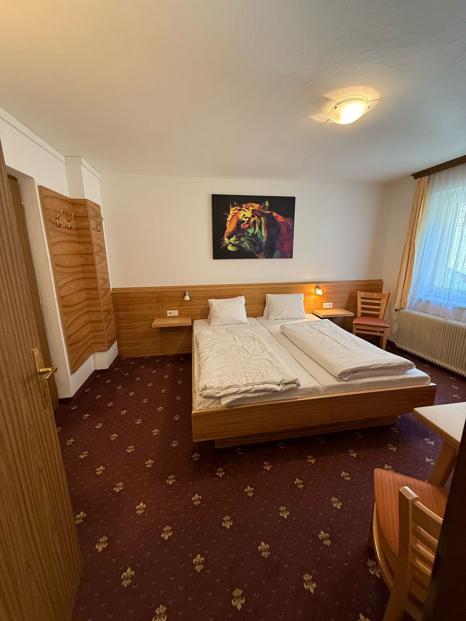 Une chambre d’hôtel avec un lit, une armoire en bois, un tableau représentant un tigre, une table de chevet et une fenêtre avec des rideaux.