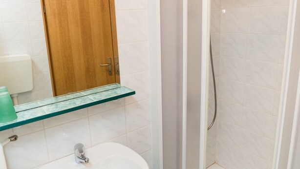 A bathroom with a wooden door, a glass shelf, a white sink, and a shower area. - Sunny Street Apartments (Rovinj)