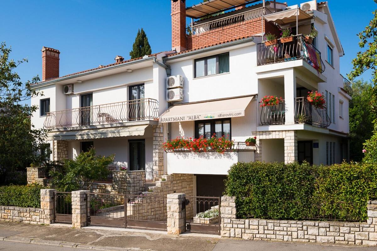 A two-story building with a sign reading "APARTMANI 'ALBA'".