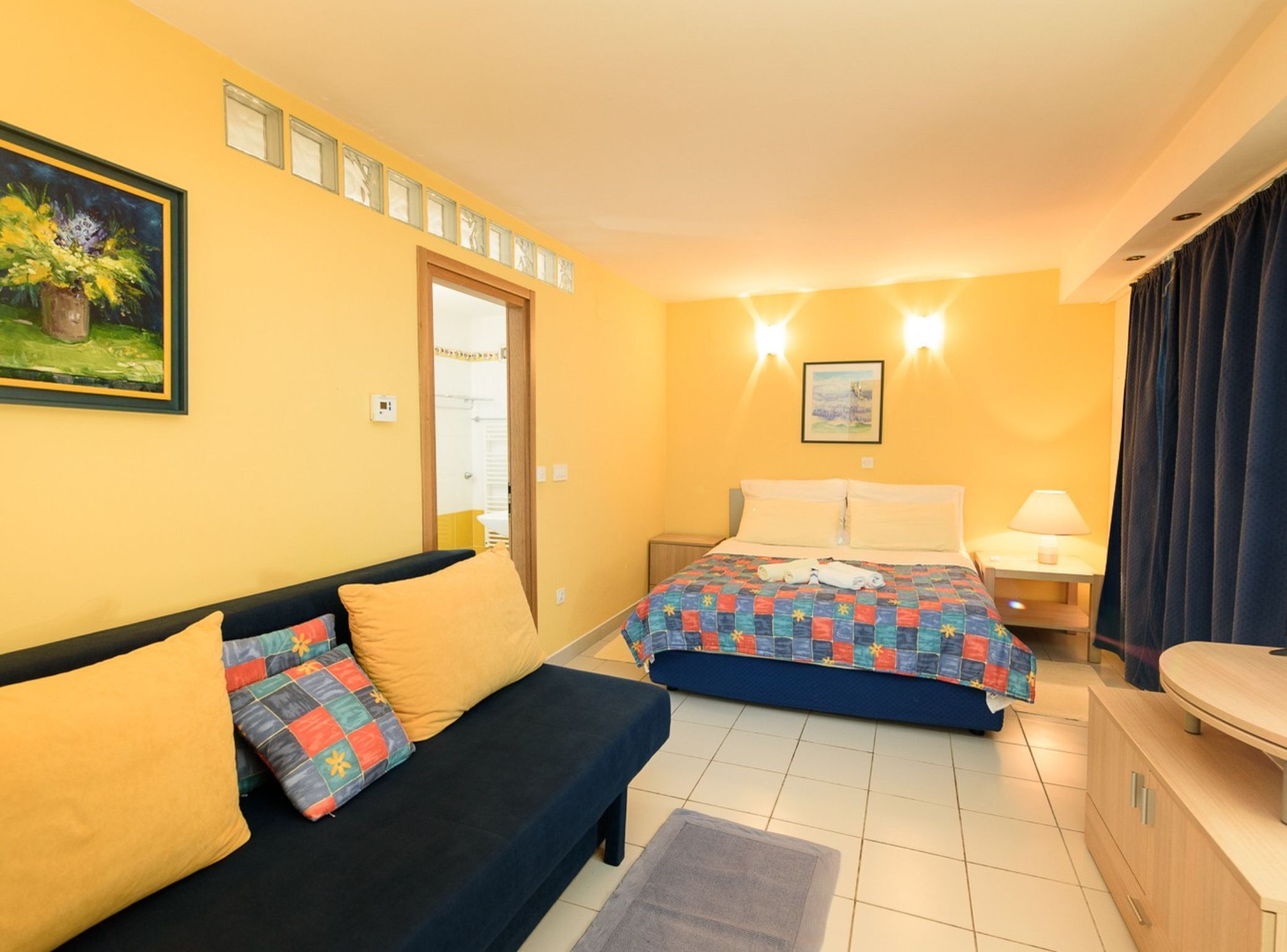 A hotel room with a bed, a sofa, a nightstand, and a painting on the wall.