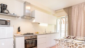 Una cocina moderna con alacenas blancas, estufa a gas, horno y microondas. Hay un comedor con sillas y una mesa blancos.
