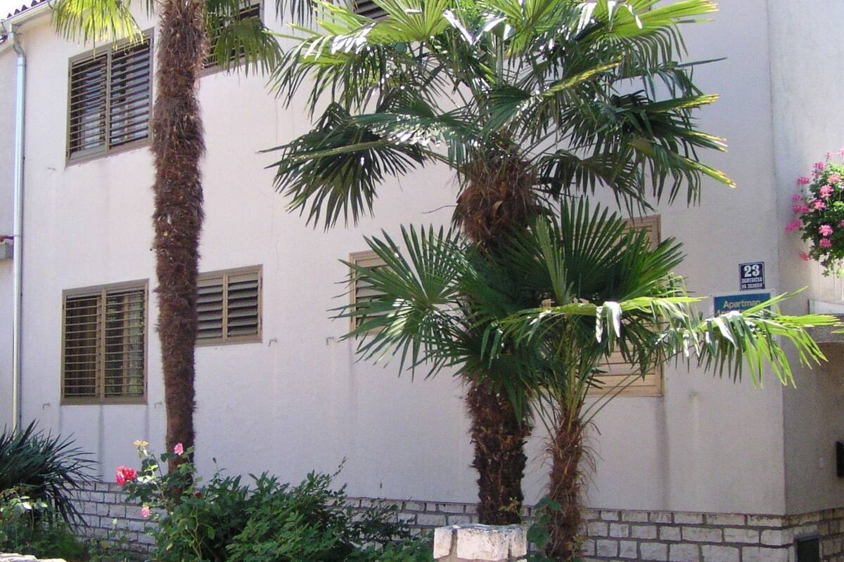 A building with a white facade, multiple windows with shutters, and a stone base.