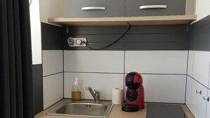 A compact kitchenette with a sink, a small refrigerator, a coffee maker, and a trash bin. - Studio SABLE & MER (Merville-Franceville-Plage)