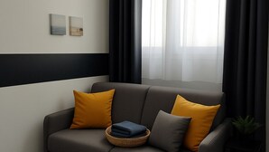 A modern living room with a grey sofa, mustard-colored cushions, and a small side table with a plant. - Studio SABLE & MER (Merville-Franceville-Plage)