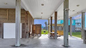 A covered outdoor area with wooden pillars, a concrete floor, and a view of colorful buildings in the background. - Abigail's House, 3 bedroom 2 bath home sleeps10. A short stroll to the beach. (Crystal Beach)