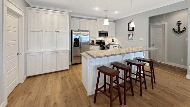 A modern kitchen with white cabinetry, a stainless steel refrigerator, a granite countertop, and a bar area with stools. - Abigail's House, 3 bedroom 2 bath home sleeps10. A short stroll to the beach. (Crystal Beach)