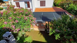 Une maison à deux étages, avec un toit recouvert de tuiles, une antenne parabolique et un petit jardin agrémenté de plantes à fleurs roses.