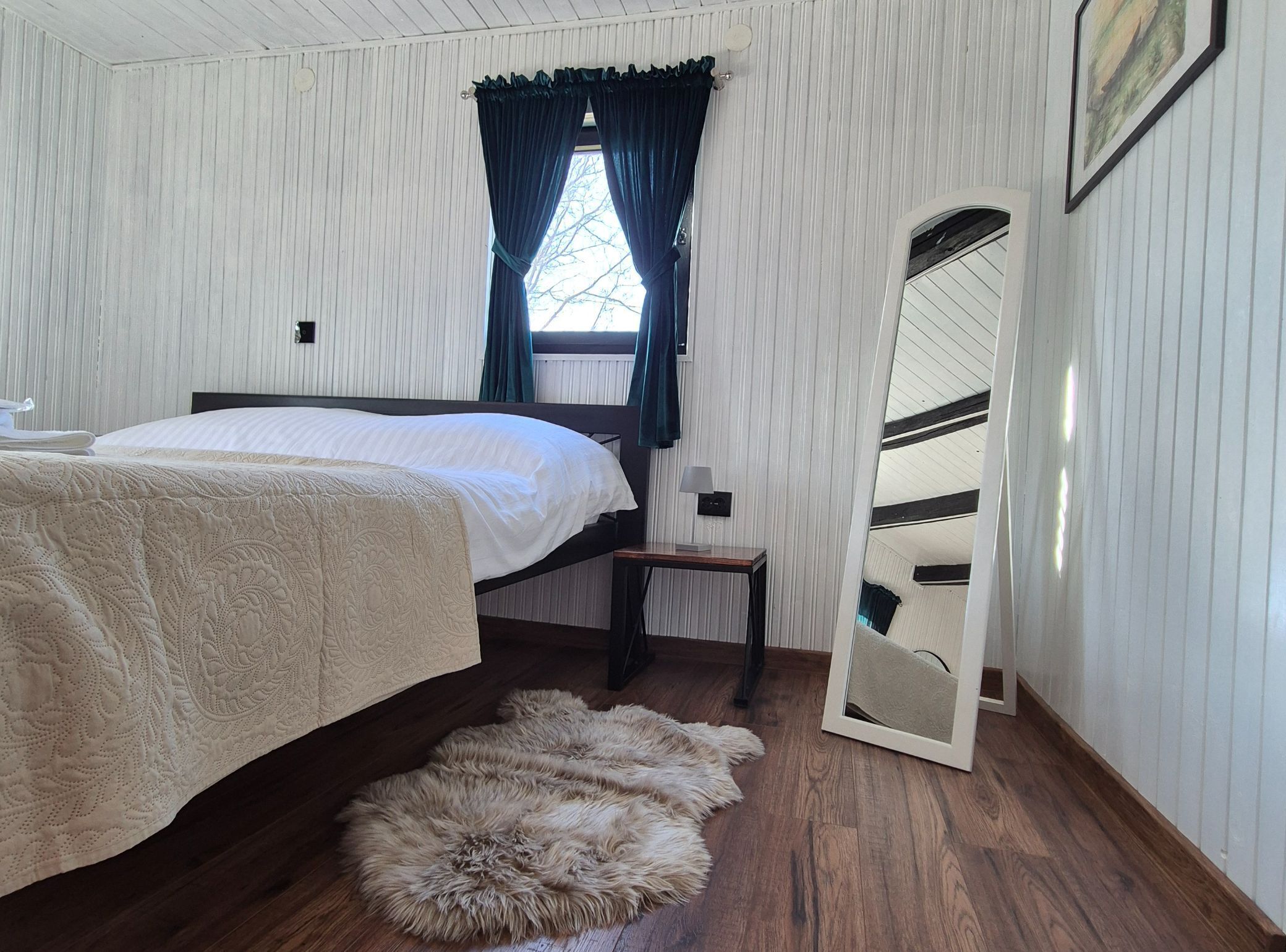 Un dormitorio con una cama, un espejo, suelo de madera y un manto de piel.