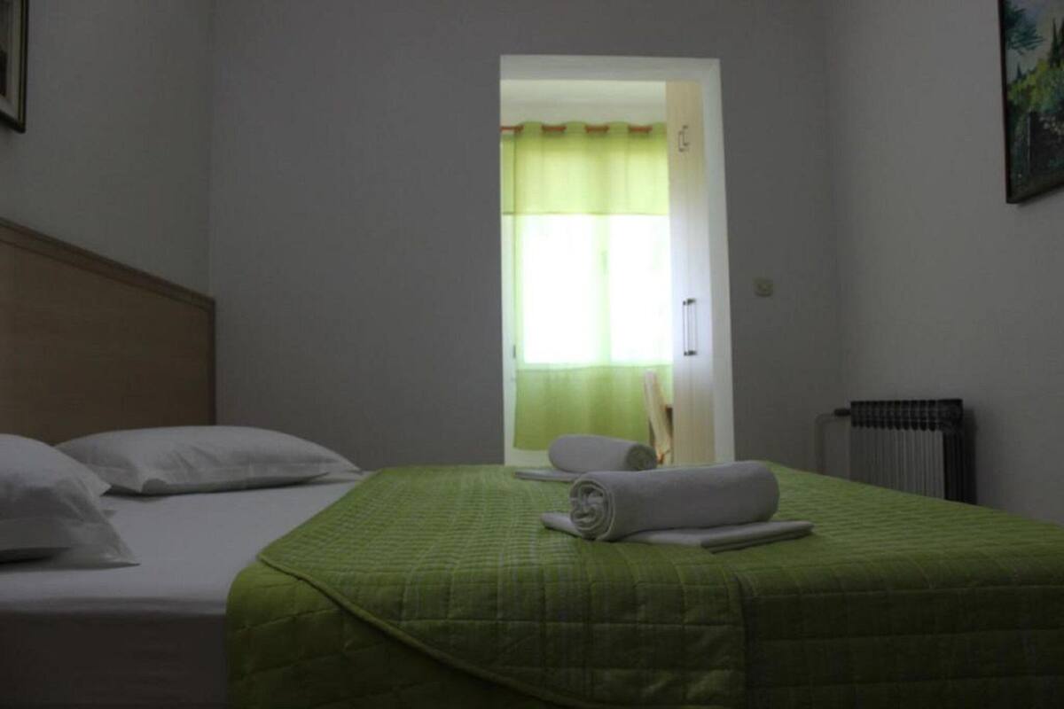 A hotel room with two beds, a green quilted bedspread, a rolled towel, and a radiator.
