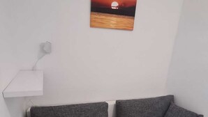 Un sofá blanco con cojines grises en una habitación con una pared blanca y un cuadro de un atardecer.