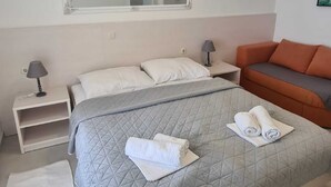 Habitación de hotel con una cama grande, una mesita de noche, una lámpara, un sofá, un espejo y un aire acondicionado instalado en la pared.