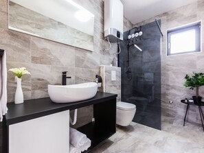 A modern bathroom with a white vessel sink, black countertop, and a glass-enclosed shower.