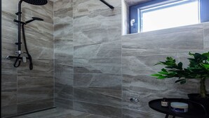 Eine Dusche mit Handbrause und Regendusche, ein Blumentopf sowie ein kleiner Tisch mit einem Behälter darauf.