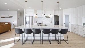 A modern kitchen with a large island, bar stools, white cabinetry, and pendant lighting. - Beautiful Lakefront Home with Spa and 6 Bedrooms! (Moses Lake)