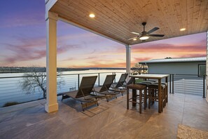 Un patio couvert avec vue sur un lac, comprenant des chaises longues et une table.