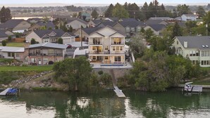 A large two-story house with a balcony, a dock, and a boat. - Beautiful Lakefront Home with Spa and 6 Bedrooms! (Moses Lake)