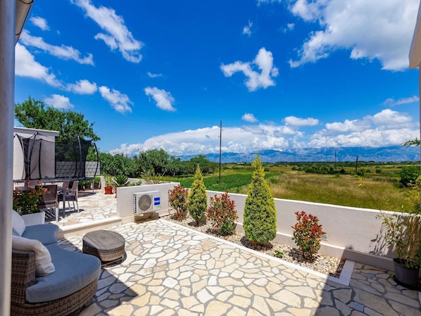 A patio with outdoor furniture, a view of mountains, and a clear sky.