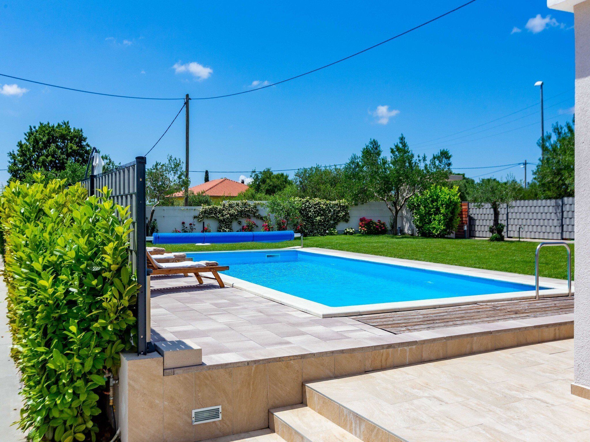 A rectangular swimming pool with a tiled deck, surrounded by a low wall and a metal fence.