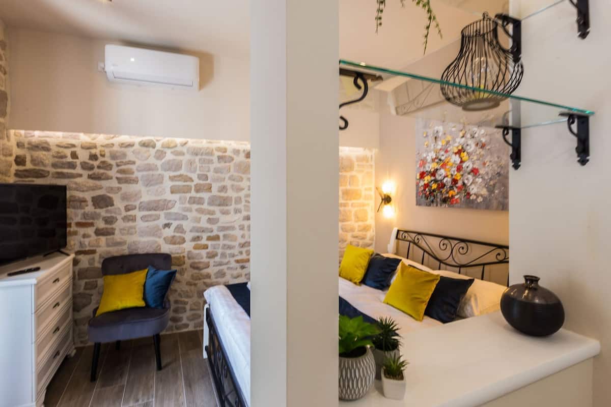 A room with a stone wall, a bed with yellow and blue pillows, a TV, and a wall-mounted light fixture.