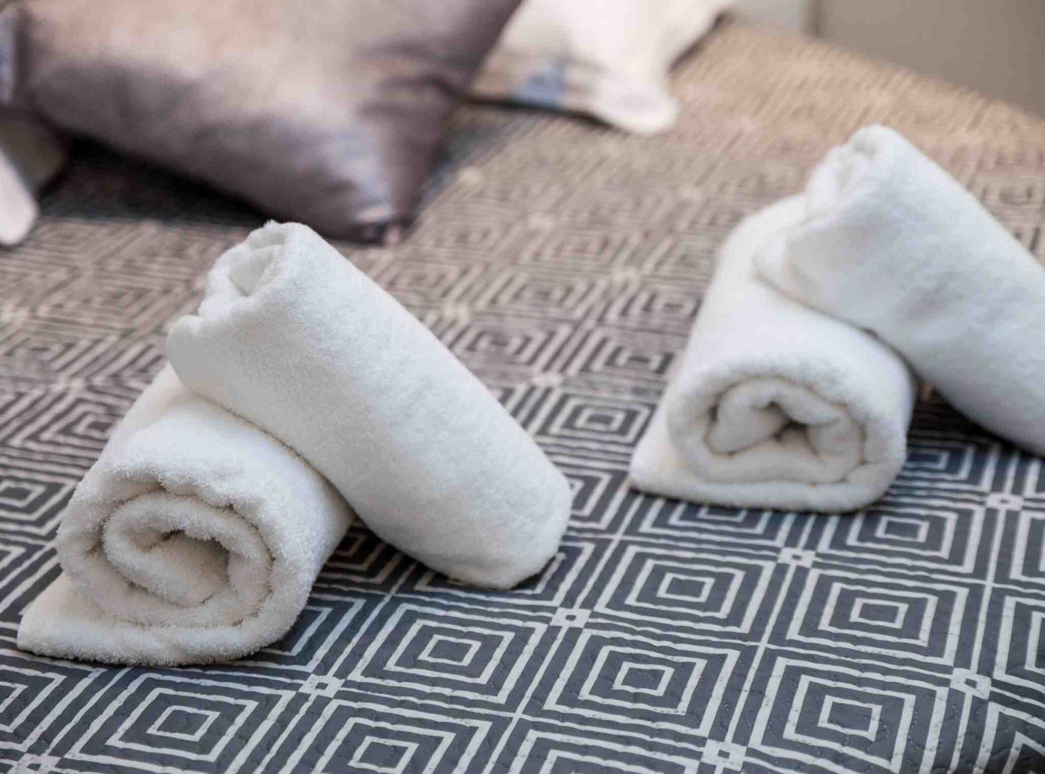 A patterned bedspread with rolled white towels placed on it.