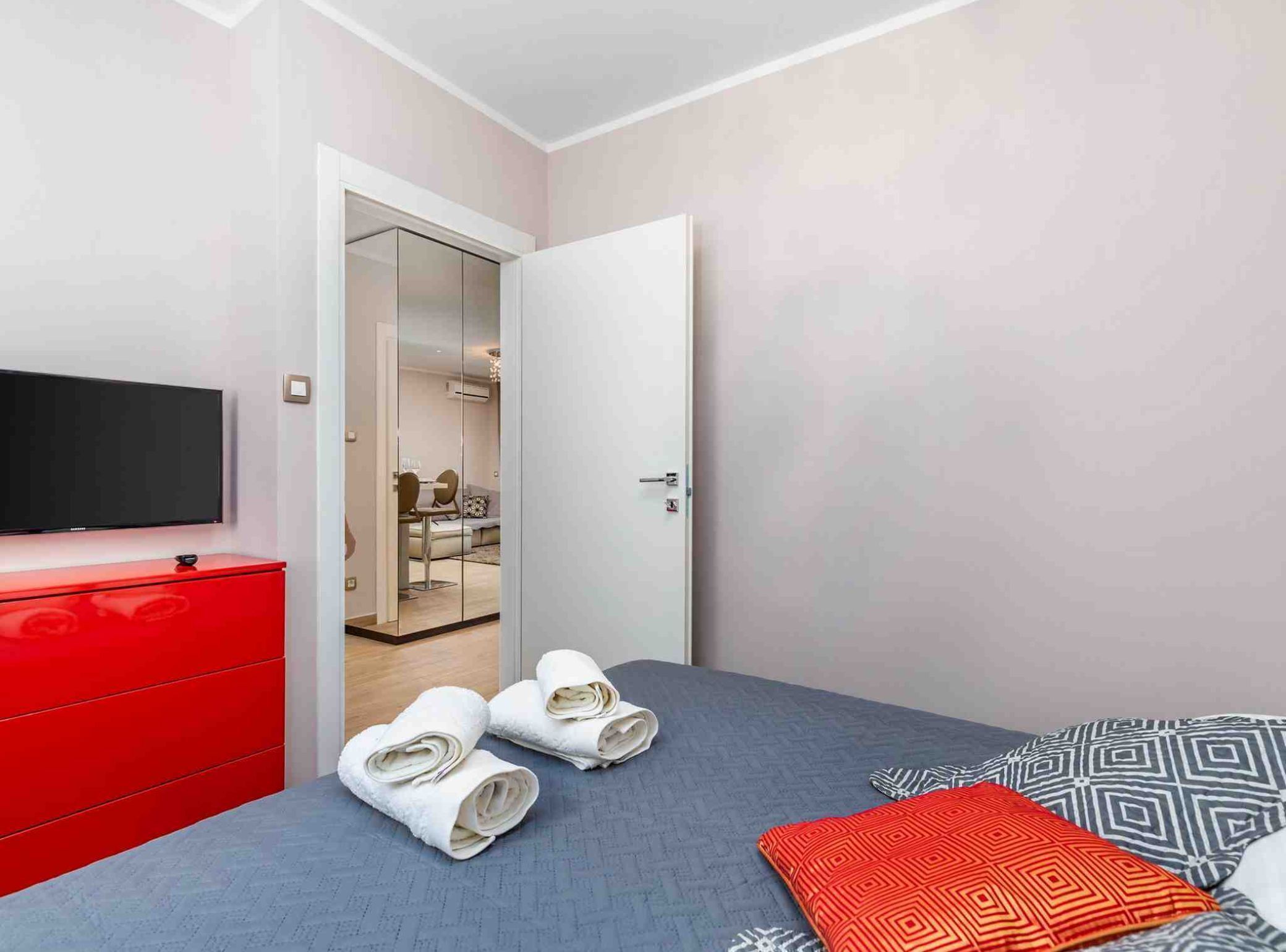A hotel room with a bed, a red dresser, a television, and a bathroom visible through an open door.