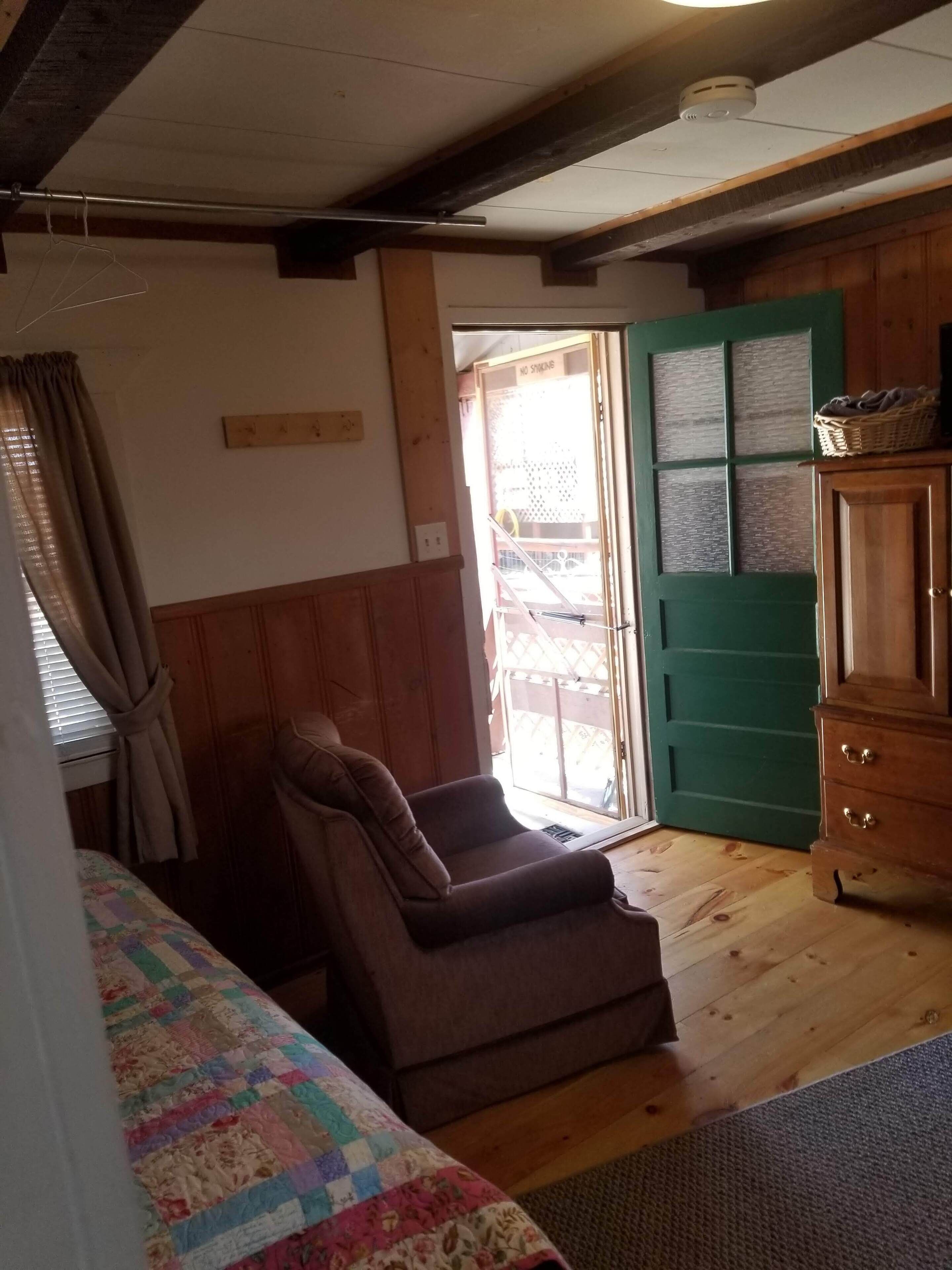 Ein Zimmer mit braunem Sofa, einem gesteppten Bett, einem Holzkasten und einer grünen Tür.