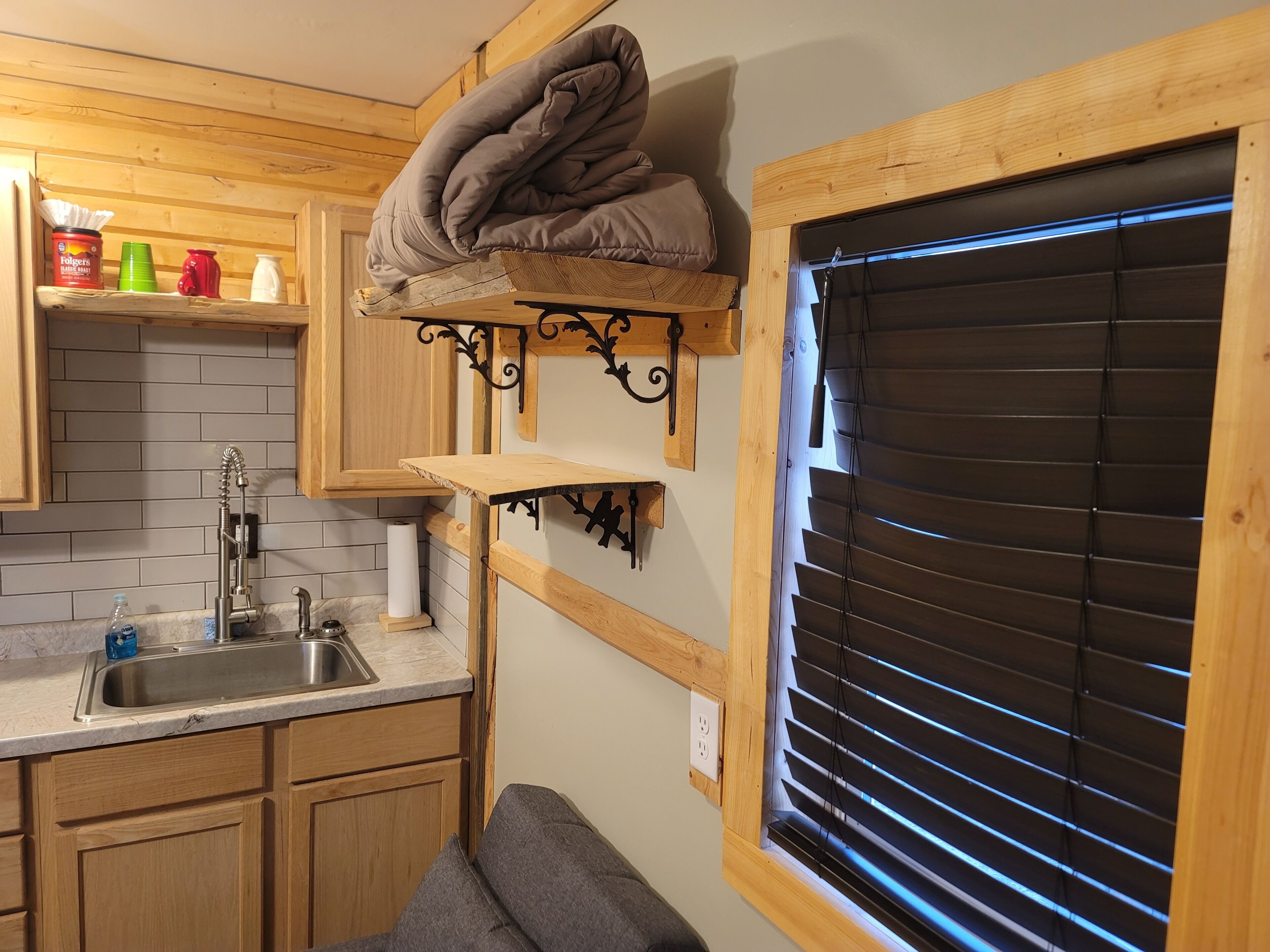 A compact kitchen with wooden cabinets, a sink, and a window with blinds.