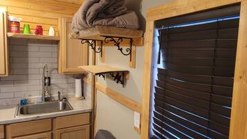 A compact kitchen with wooden cabinets, a sink, and a window with blinds.