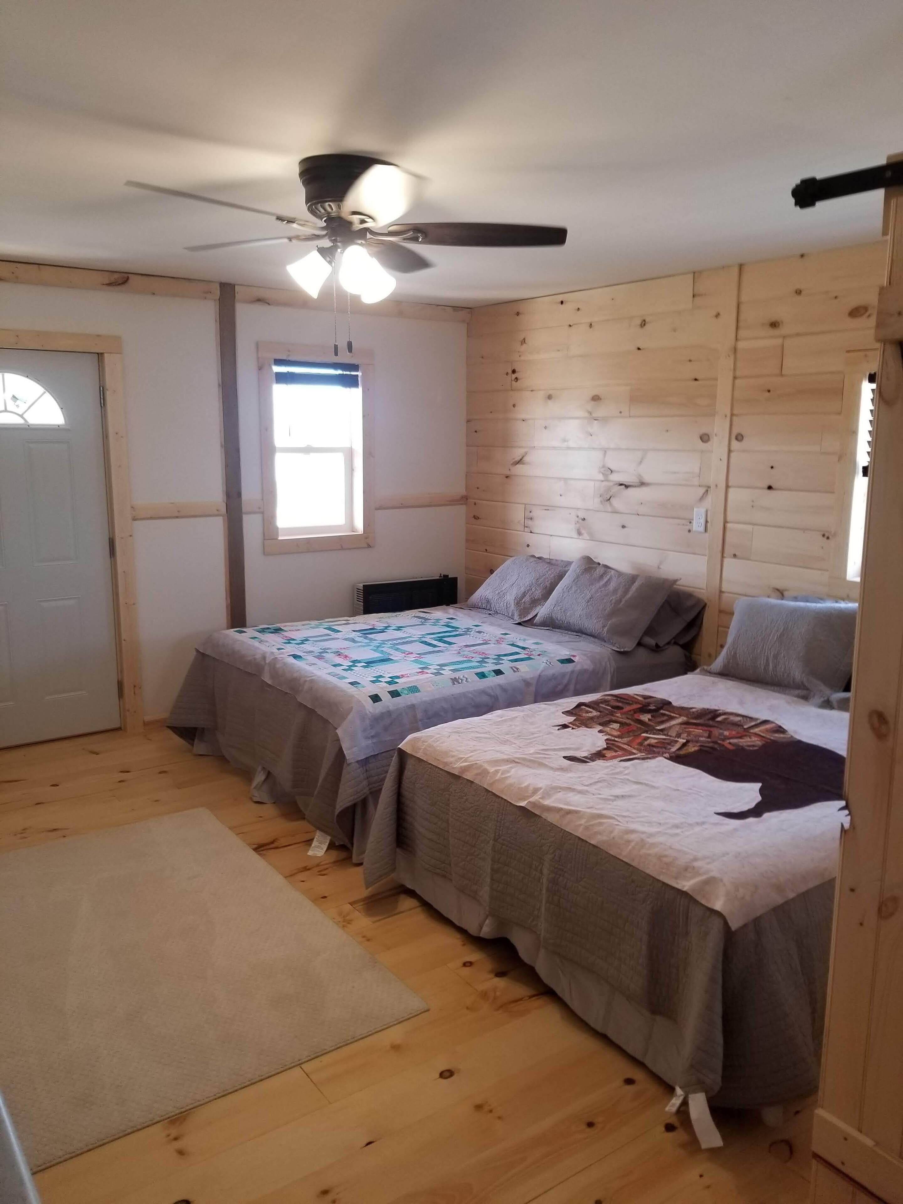 A bedroom with two beds, a ceiling fan, a window, and a door.