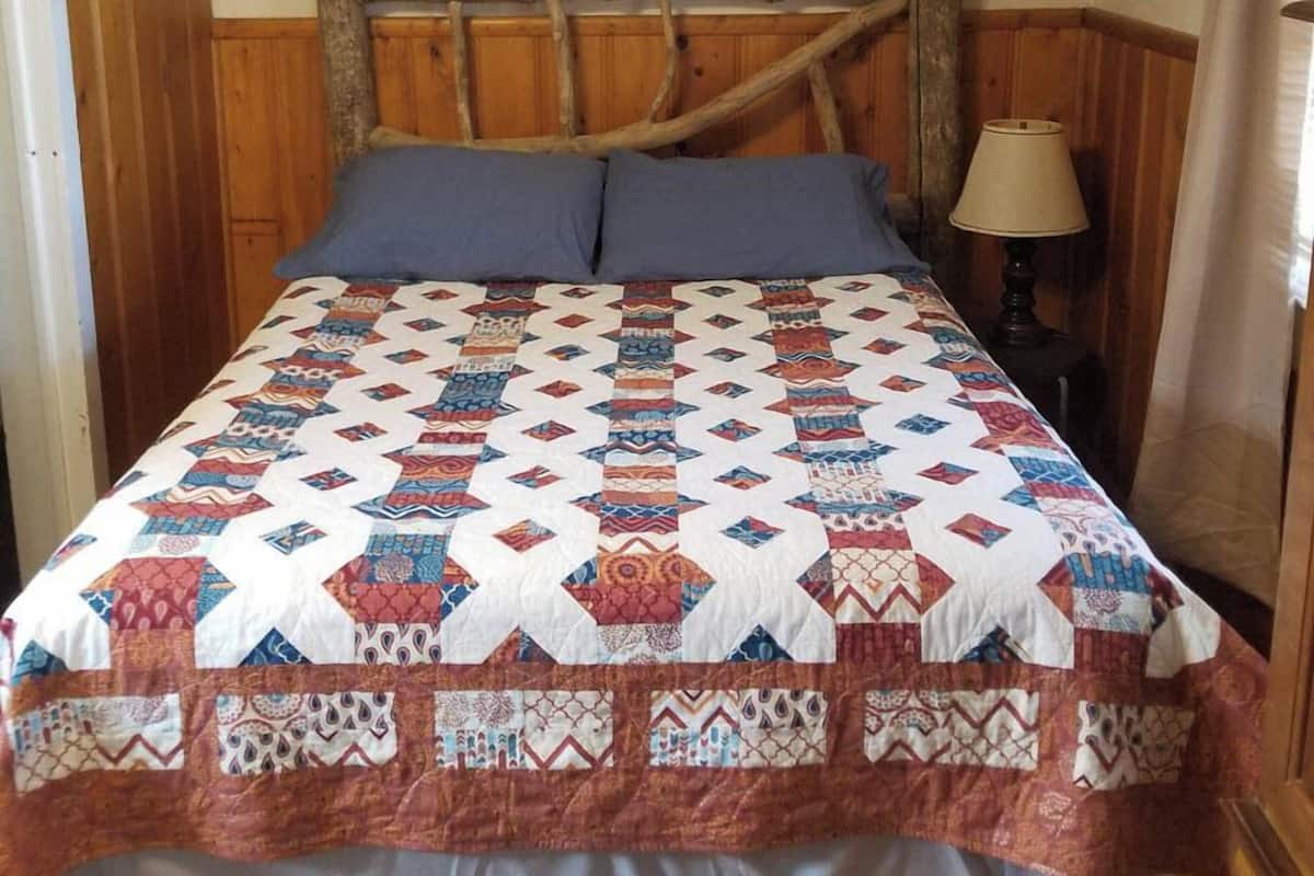 A bed with a wooden headboard, a quilt, and a bedside lamp.