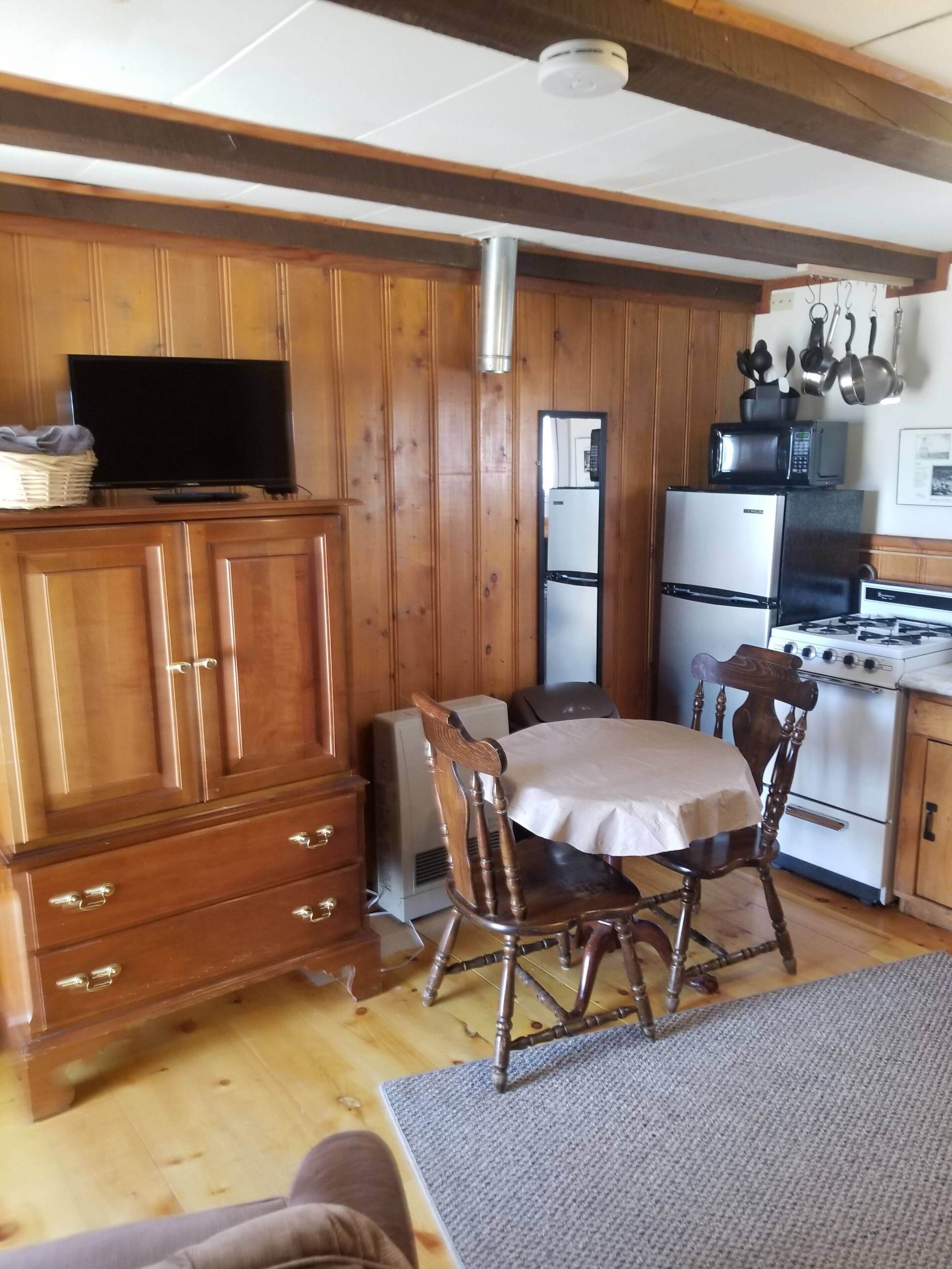 A compact kitchen with wooden cabinets, a refrigerator, a microwave, a stove, and a dining table with chairs.