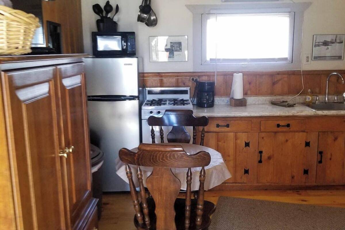A compact kitchen with wooden cabinets, a gas stove, a refrigerator, and a window providing natural light.