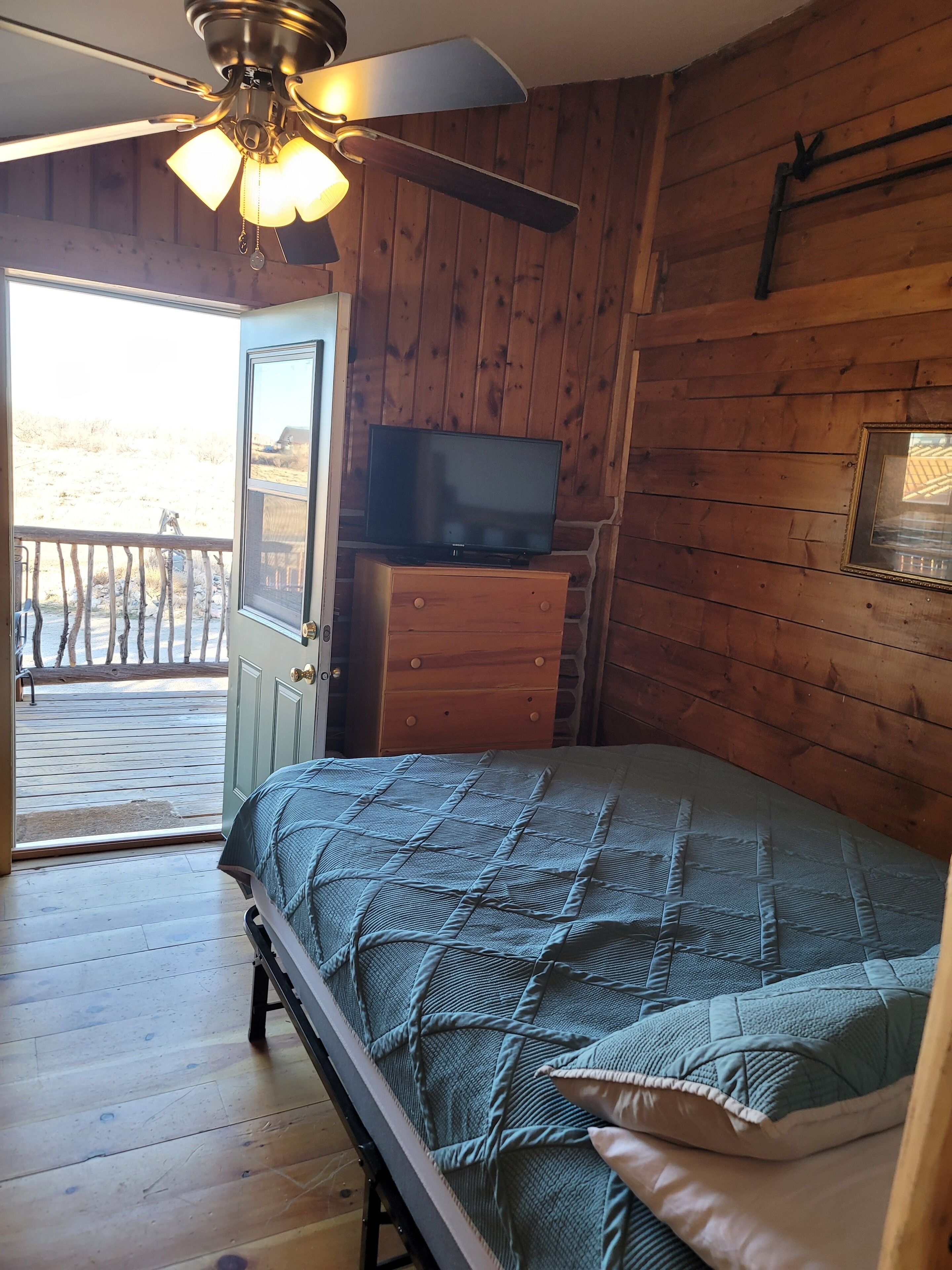 Un dormitorio con cama, televisor en una cómoda y balcón con barandilla de madera.