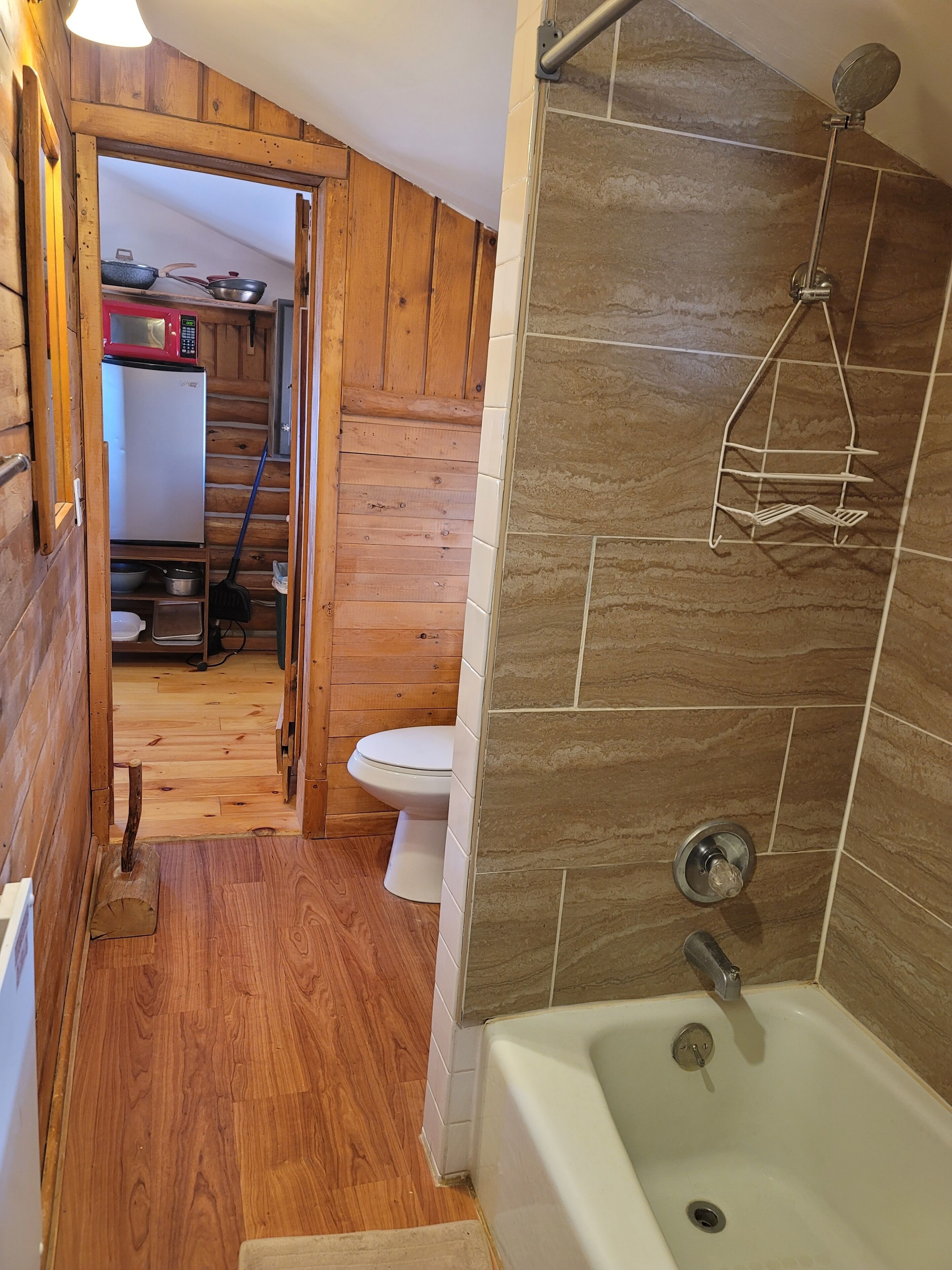 A wooden cabin bathroom with a bathtub, a shower, and a toilet.