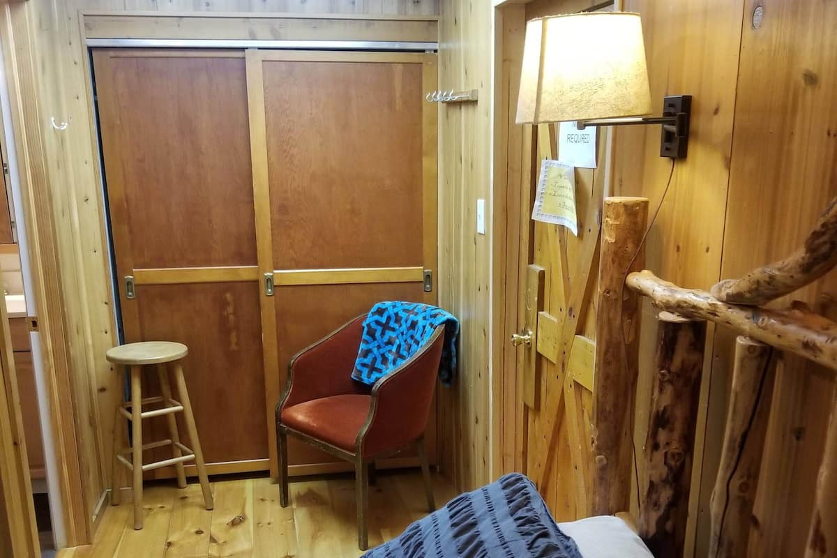 A wooden cabin room with a bed, a chair, a ladder, and a door.