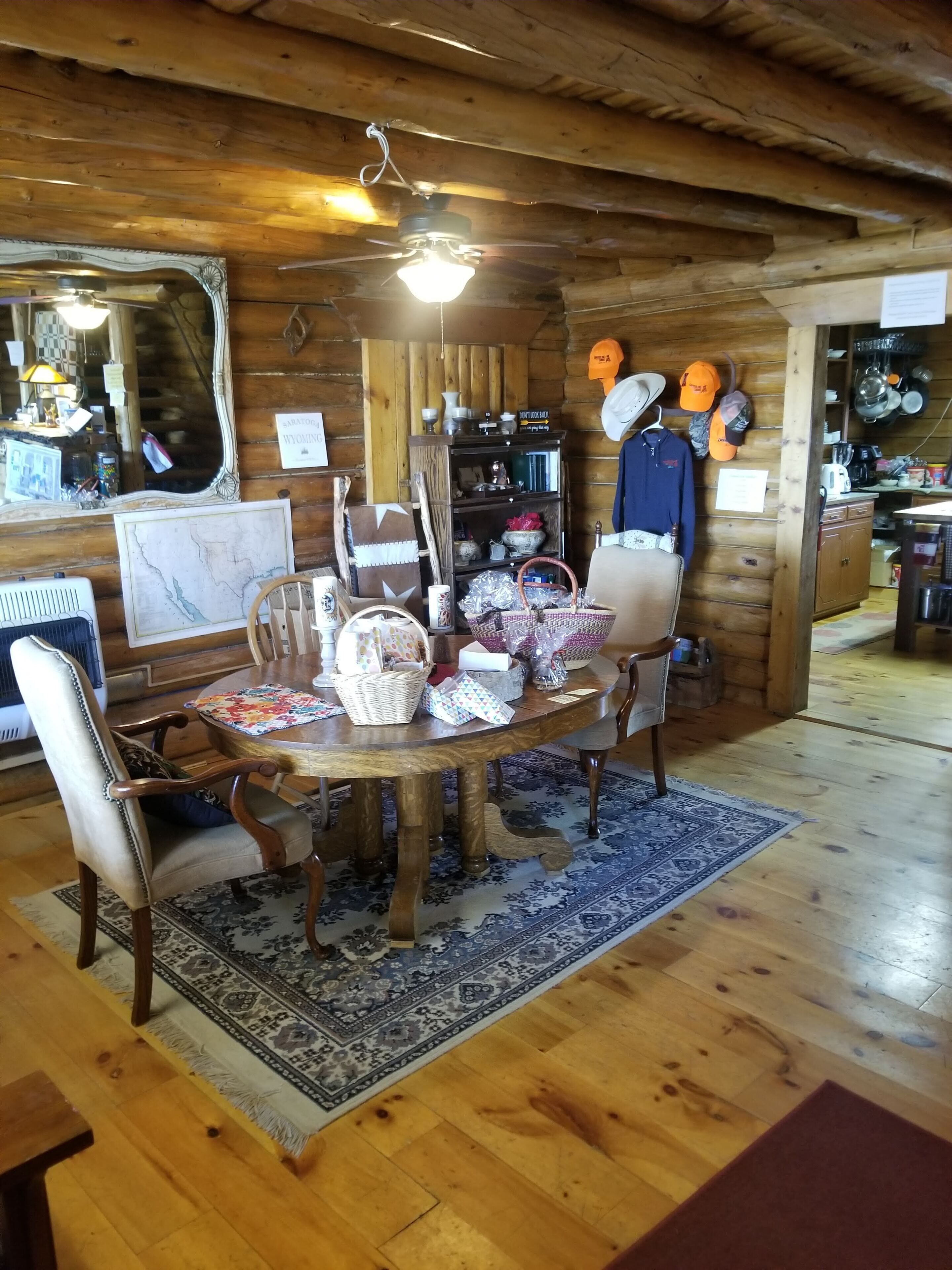 A wooden interior with a dining table, chairs, a ceiling fan, and a kitchen area with shelves and hanging items.