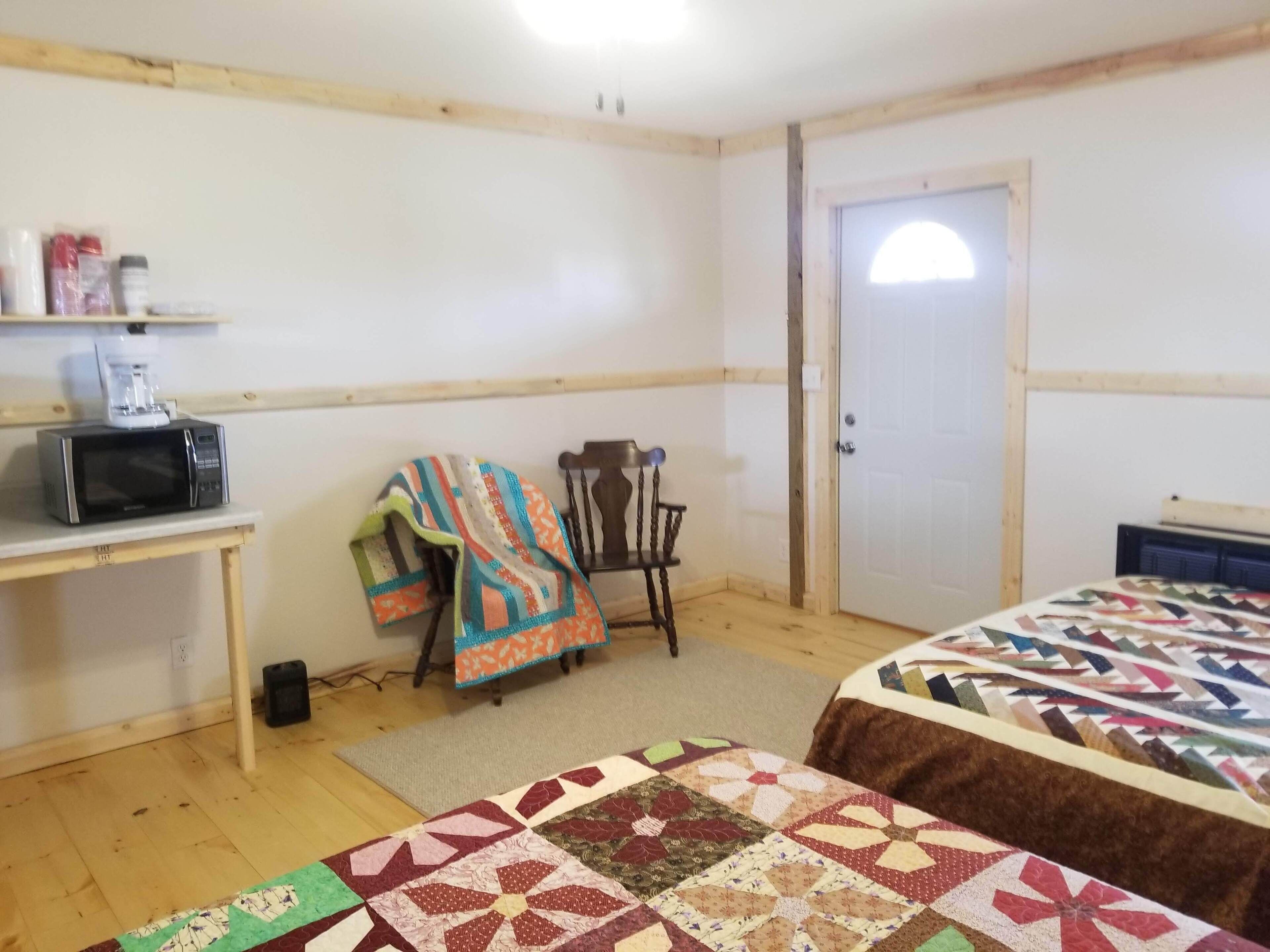 A room with a bed, a chair, a desk with a microwave, and a door.