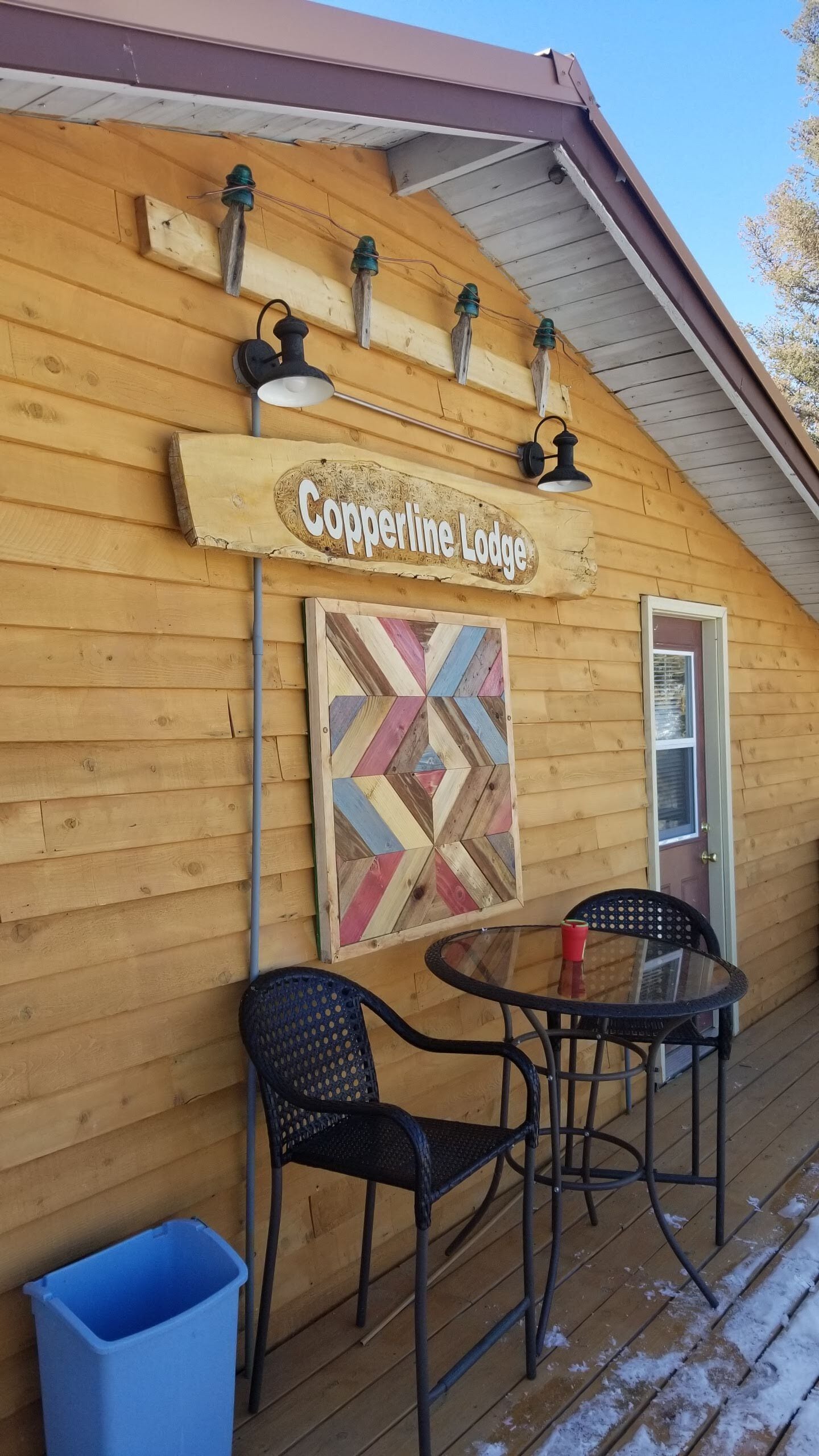 A wooden cabin with a sign reading "Copperline Lodge" and a decorative geometric wall art piece.