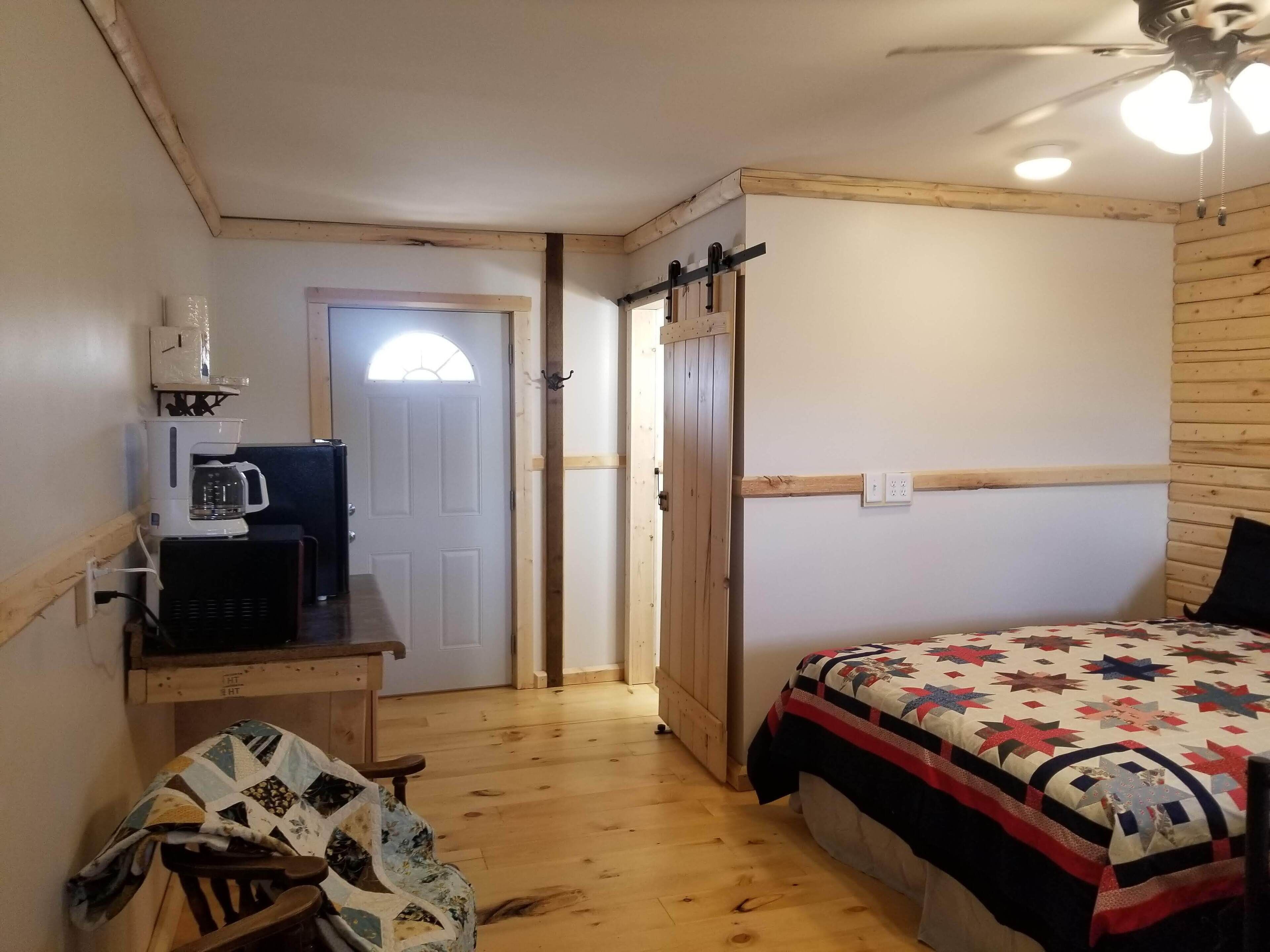 Une chambre comprenant un lit, une machine à café, un bureau et une porte donnant sur une autre pièce.