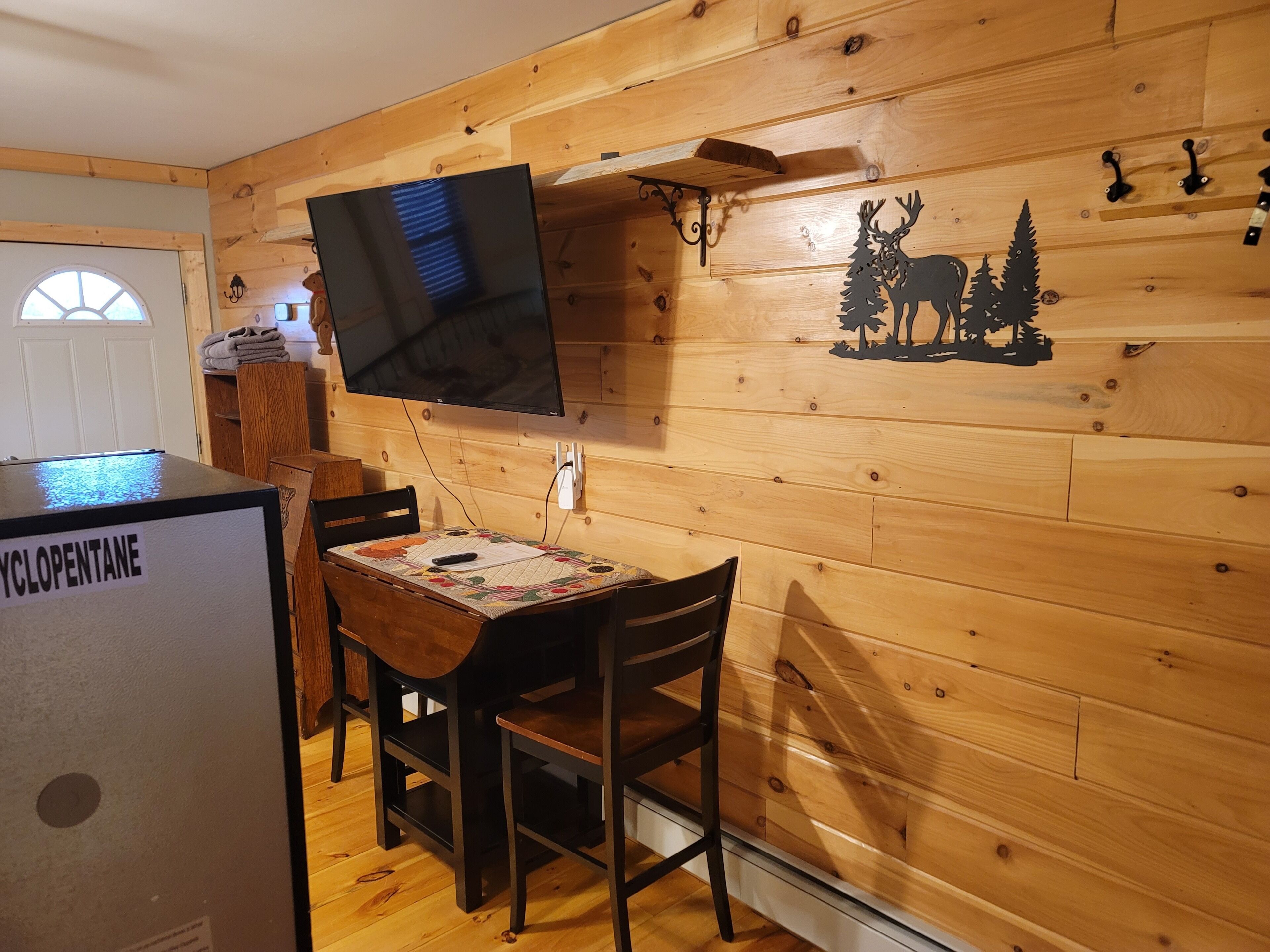 A wooden interior with a dining area, a television mounted on the wall, and a refrigerator labeled "CYCLOPENTANE".