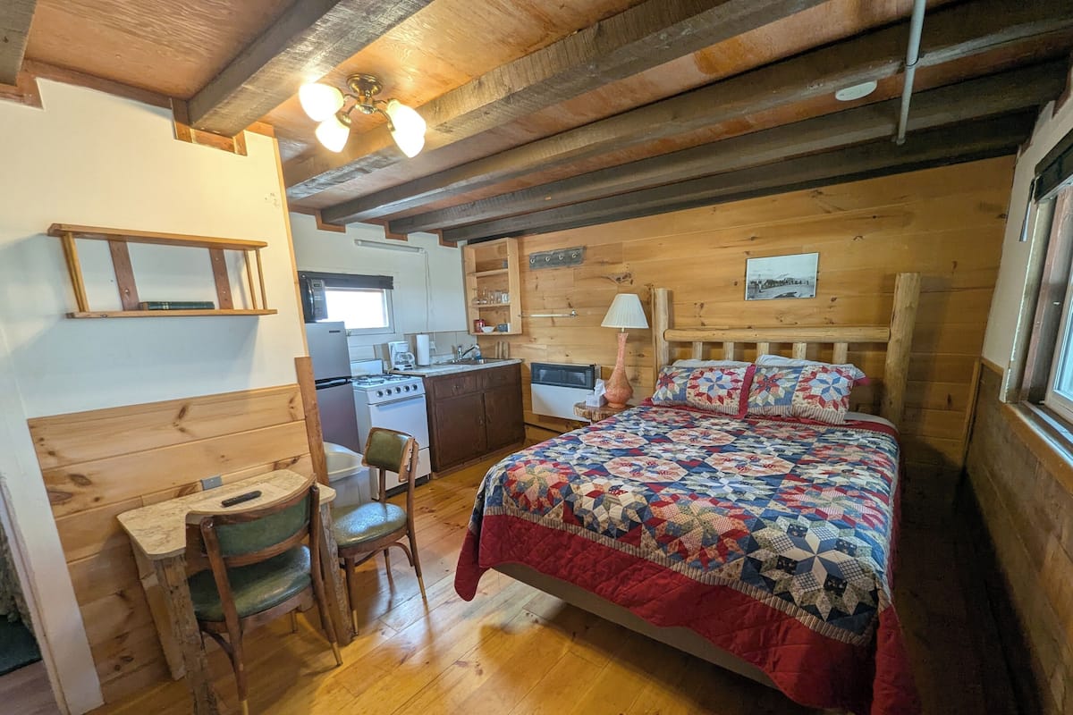 A cozy cabin-style room with a wooden bed, a desk, and a kitchenette.