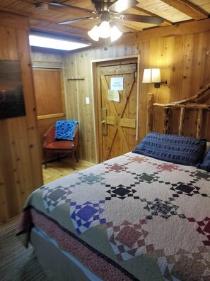 A wooden room with a bed, a chair, a door with a sign, and a ceiling fan. - CopperLine Lodge (Saratoga)